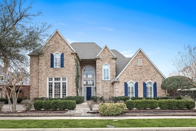 traditional home featuring roof with shingles and brick siding