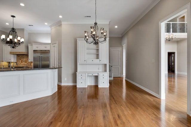 interior space with tasteful backsplash, white cabinets, open shelves, a notable chandelier, and built in fridge