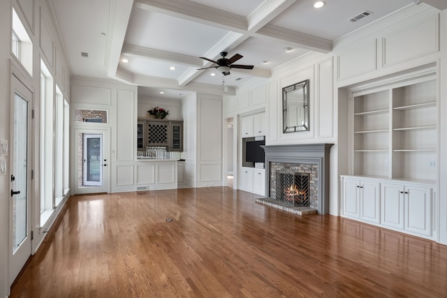 unfurnished living room with built in shelves, coffered ceiling, visible vents, a brick fireplace, and beam ceiling