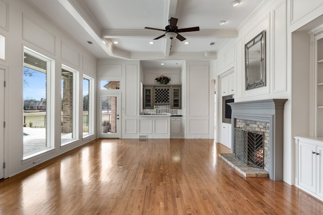 unfurnished living room with ceiling fan, light wood-style floors, ornamental molding, a brick fireplace, and beamed ceiling