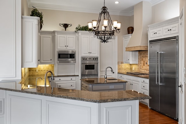 kitchen with built in appliances, a peninsula, crown molding, premium range hood, and a sink