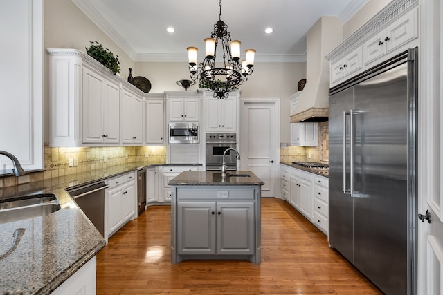 kitchen featuring built in appliances, a sink, white cabinets, ornamental molding, and light wood finished floors