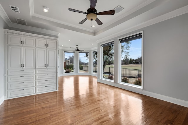 unfurnished bedroom with light wood finished floors, baseboards, visible vents, a raised ceiling, and crown molding