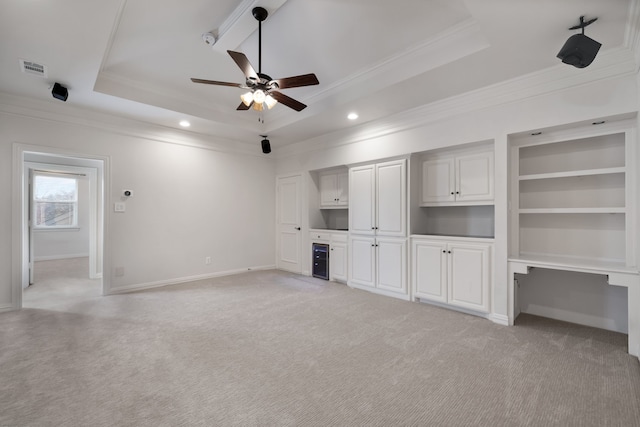 unfurnished living room with a raised ceiling, built in study area, and light carpet