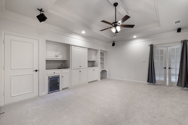 unfurnished living room featuring light carpet, wine cooler, a tray ceiling, and ornamental molding