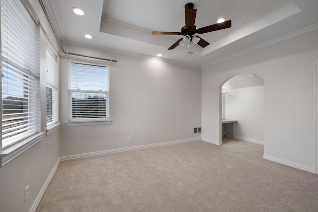 unfurnished room featuring arched walkways, a raised ceiling, ornamental molding, carpet flooring, and baseboards