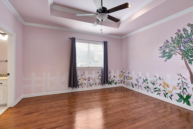 empty room featuring crown molding, a tray ceiling, ceiling fan, and light wood finished floors