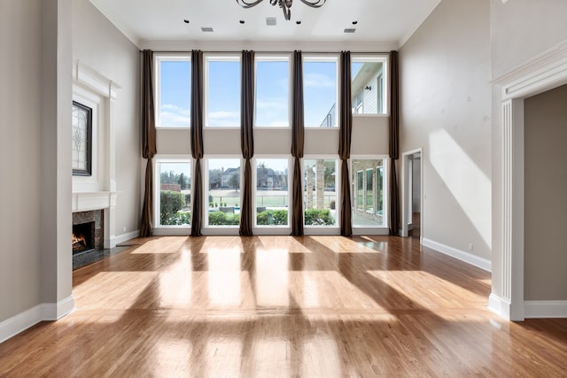 unfurnished living room with a fireplace, crown molding, a towering ceiling, and wood finished floors