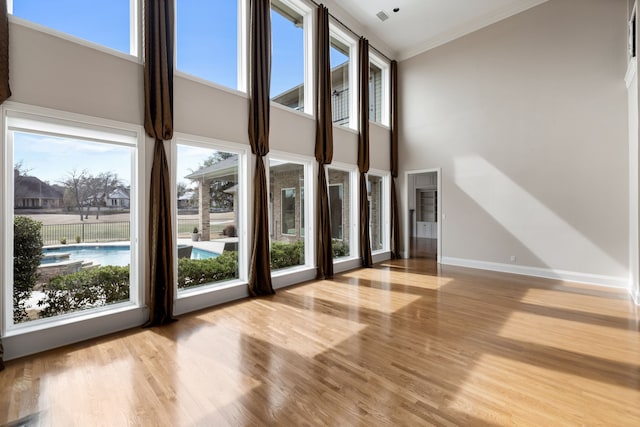 interior space featuring a high ceiling, crown molding, baseboards, and wood finished floors