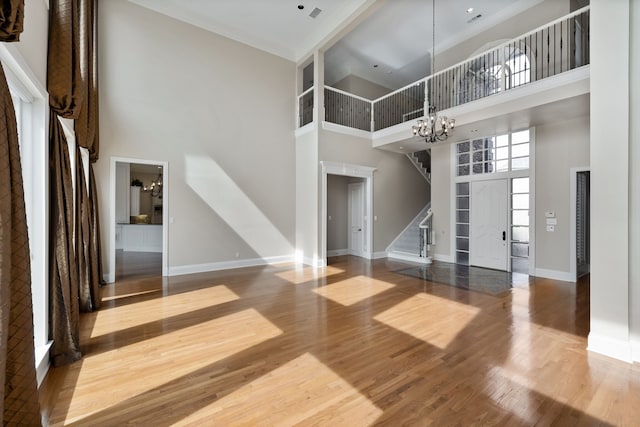 unfurnished living room featuring wood finished floors, visible vents, baseboards, stairway, and an inviting chandelier