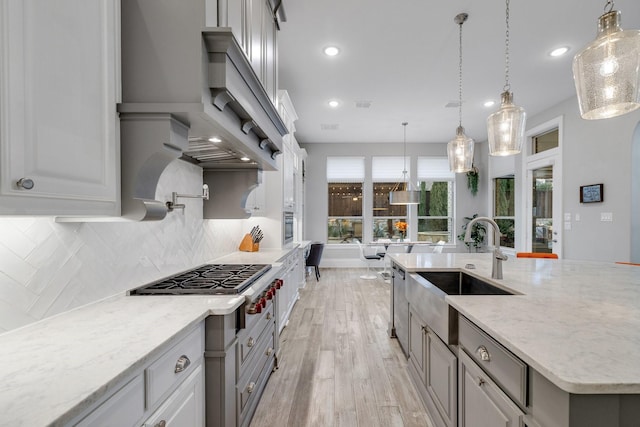 kitchen with light stone counters, light wood-style flooring, a sink, decorative backsplash, and stainless steel gas stovetop