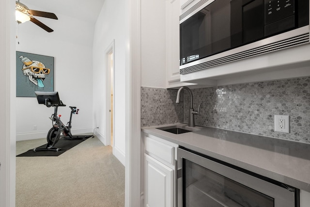 kitchen with beverage cooler, tasteful backsplash, stainless steel microwave, carpet floors, and white cabinetry