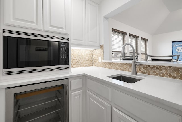 kitchen with built in microwave, beverage cooler, white cabinets, and a sink