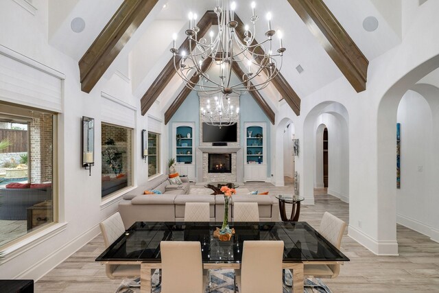 dining room featuring a warm lit fireplace, light wood-style flooring, built in shelves, high vaulted ceiling, and beam ceiling