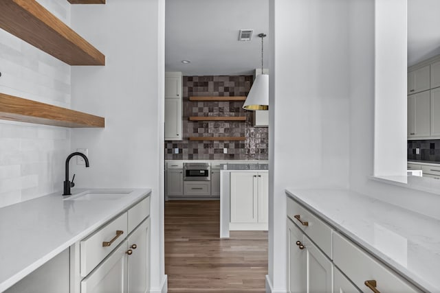 kitchen with visible vents, decorative backsplash, wood finished floors, open shelves, and a sink