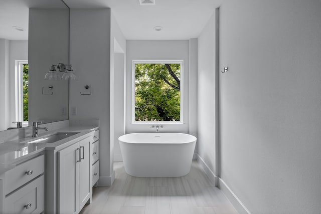 bathroom featuring visible vents, a freestanding tub, vanity, and baseboards