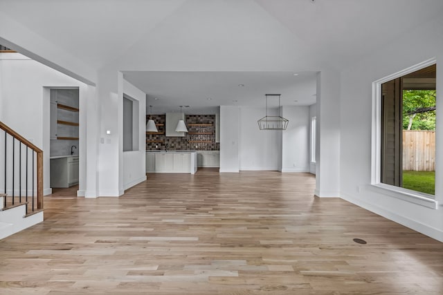 unfurnished living room featuring vaulted ceiling, stairway, and light wood-style floors