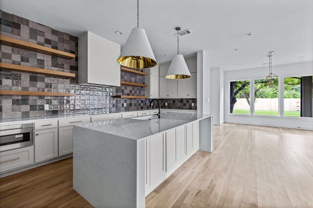 kitchen featuring tasteful backsplash, visible vents, light wood-style flooring, a kitchen island with sink, and open shelves