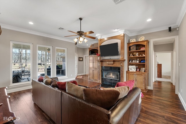 living area with dark wood-style flooring, a tiled fireplace, visible vents, and crown molding