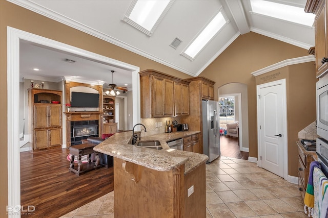 kitchen featuring visible vents, appliances with stainless steel finishes, brown cabinetry, a sink, and a peninsula