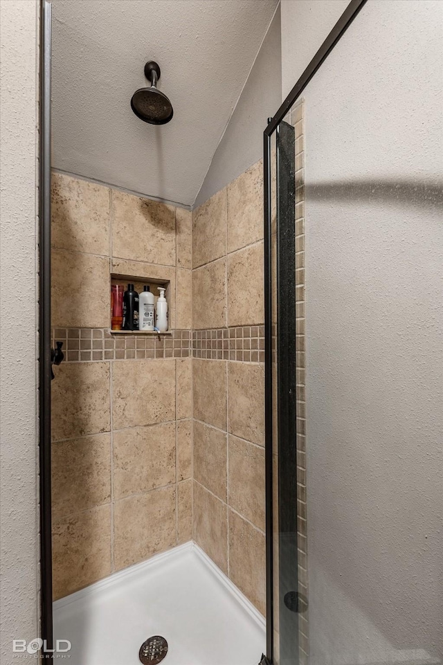 bathroom featuring a shower stall, vaulted ceiling, and a textured ceiling