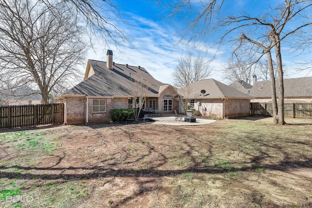 rear view of house featuring a patio area, a fenced backyard, a chimney, and brick siding