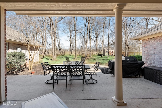 view of patio with an outbuilding, grilling area, outdoor dining space, fence, and a shed