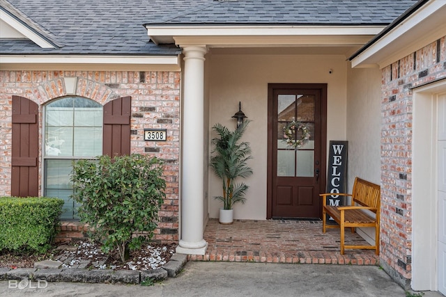 entrance to property featuring covered porch, brick siding, and roof with shingles