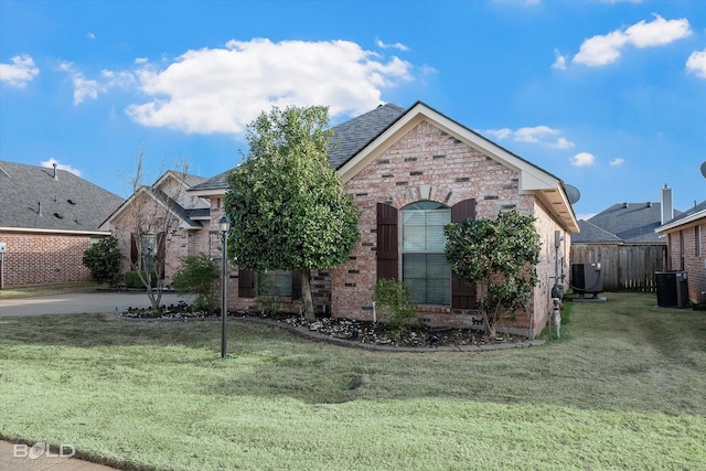 view of front facade with brick siding, fence, cooling unit, and a front yard