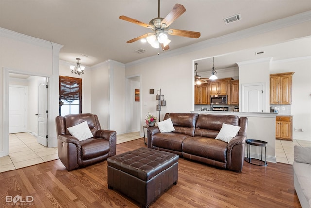 living area with ceiling fan with notable chandelier, light wood-type flooring, visible vents, and crown molding