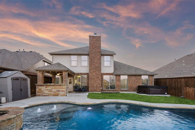 view of pool featuring outdoor dry bar, a hot tub, a storage shed, a fenced backyard, and an outbuilding