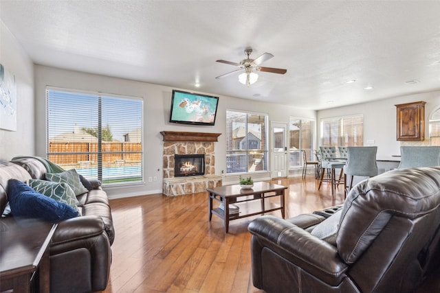 living room featuring a stone fireplace, light wood-type flooring, a wealth of natural light, and a textured ceiling