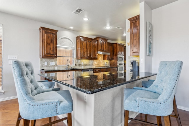 kitchen featuring visible vents, under cabinet range hood, dark stone countertops, appliances with stainless steel finishes, and a sink