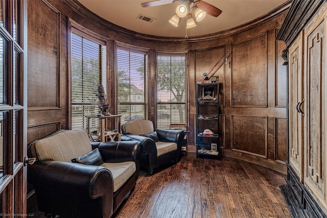 sitting room featuring ceiling fan, wooden walls, visible vents, ornamental molding, and dark wood-style floors