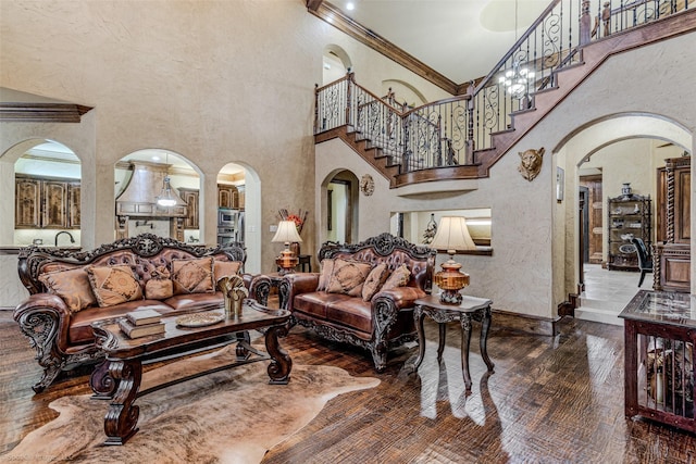 living area with arched walkways, crown molding, a high ceiling, wood finished floors, and baseboards