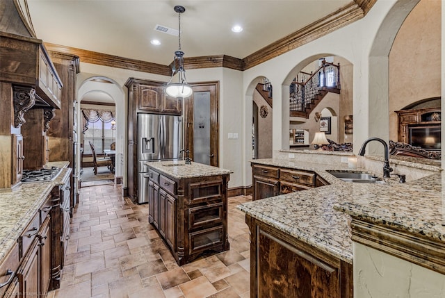 kitchen featuring arched walkways, a sink, a center island with sink, and dark brown cabinetry