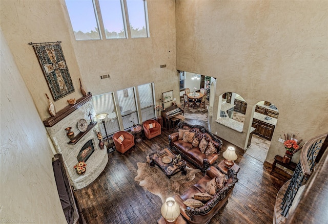 living room featuring visible vents, arched walkways, a towering ceiling, hardwood / wood-style flooring, and a lit fireplace