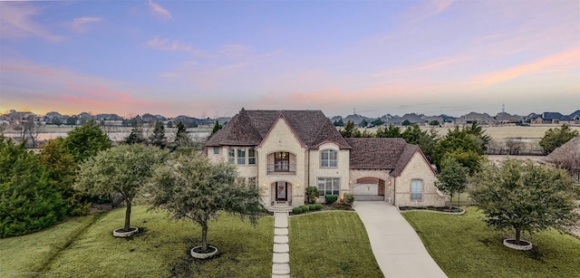 french country home featuring driveway, a front lawn, and stone siding