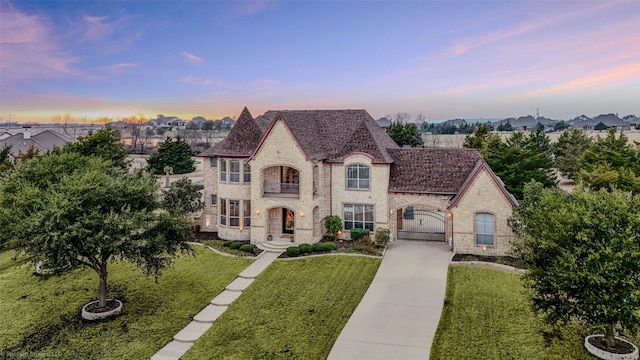 french provincial home featuring a front yard, a gate, brick siding, and concrete driveway