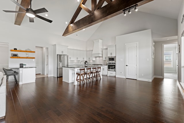 unfurnished living room featuring dark wood finished floors, ceiling fan, high vaulted ceiling, beamed ceiling, and baseboards