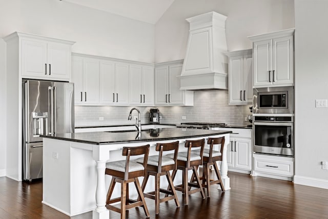 kitchen with dark wood finished floors, a breakfast bar area, custom range hood, appliances with stainless steel finishes, and a sink