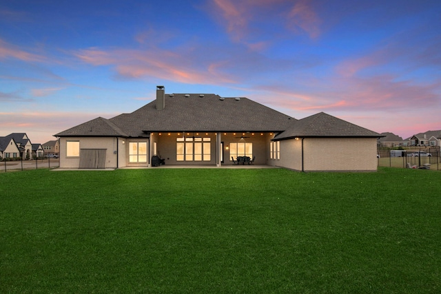 back of house at dusk featuring a yard, a chimney, a patio area, fence, and ceiling fan