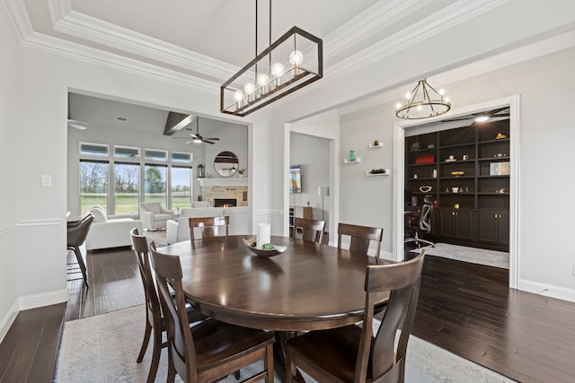 dining room featuring a lit fireplace, baseboards, wood-type flooring, and ceiling fan with notable chandelier