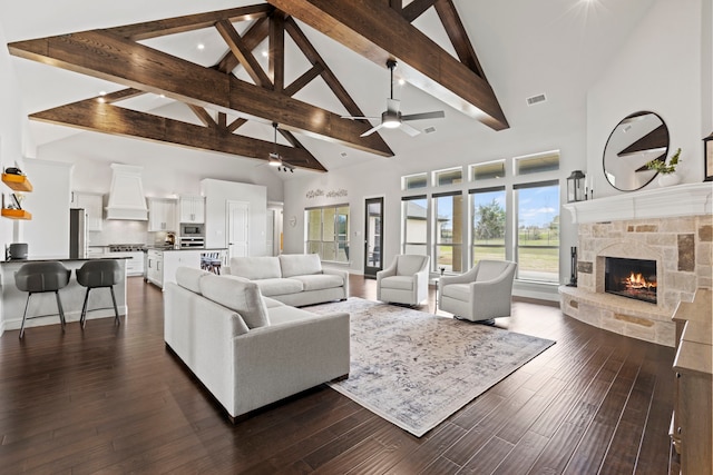 living area featuring ceiling fan, a fireplace, visible vents, dark wood-style floors, and beamed ceiling