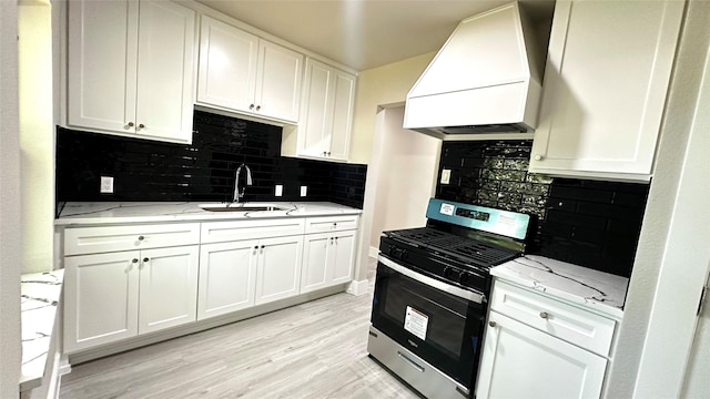 kitchen featuring stainless steel gas range oven, custom exhaust hood, white cabinets, and a sink