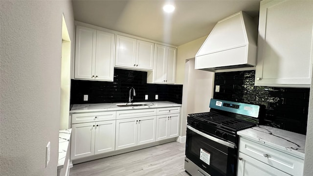 kitchen with light stone counters, custom range hood, backsplash, a sink, and gas range