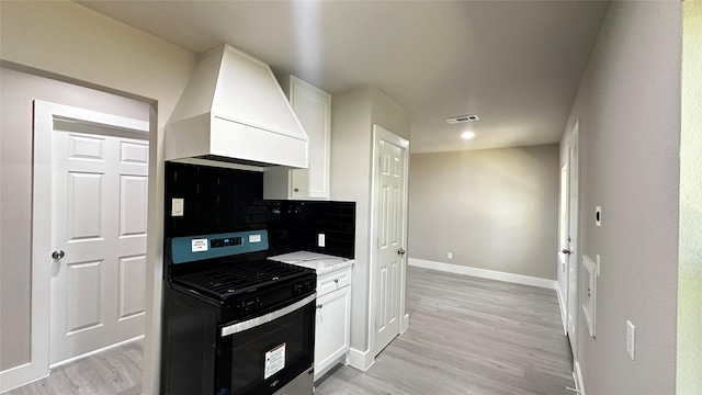 kitchen with baseboards, white cabinets, custom range hood, black range with gas stovetop, and backsplash