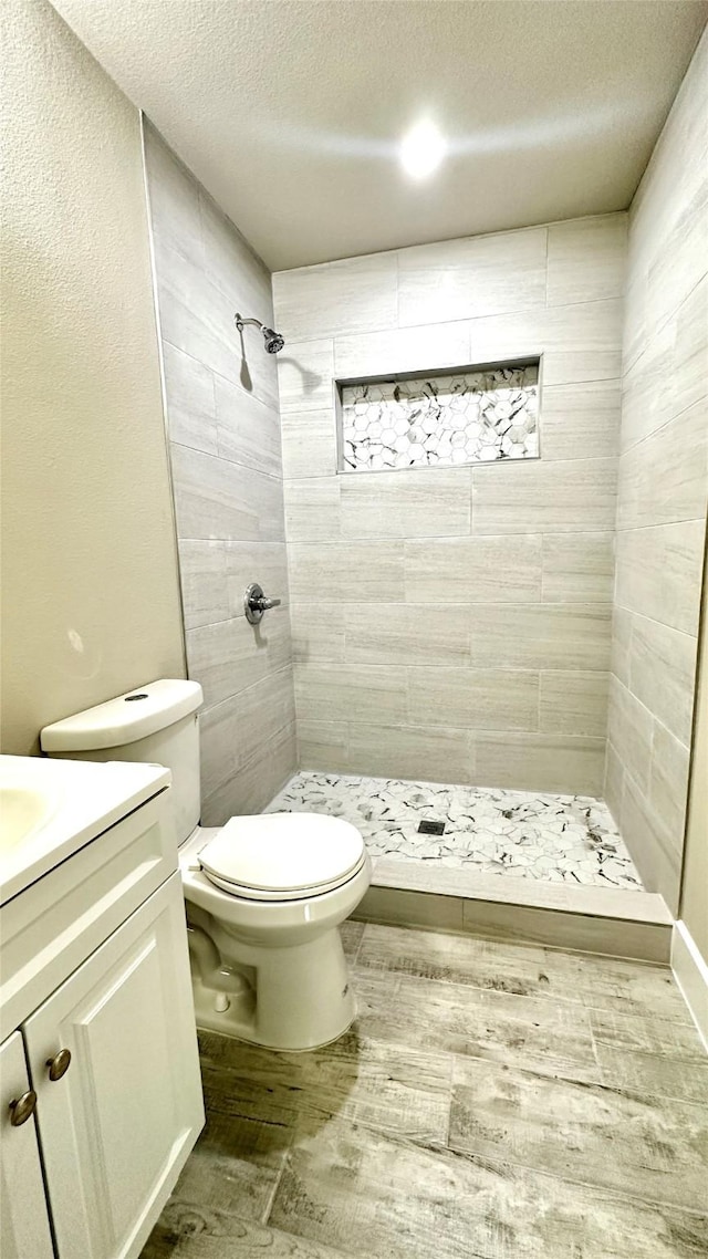 full bath featuring a textured ceiling, toilet, wood finished floors, vanity, and a stall shower