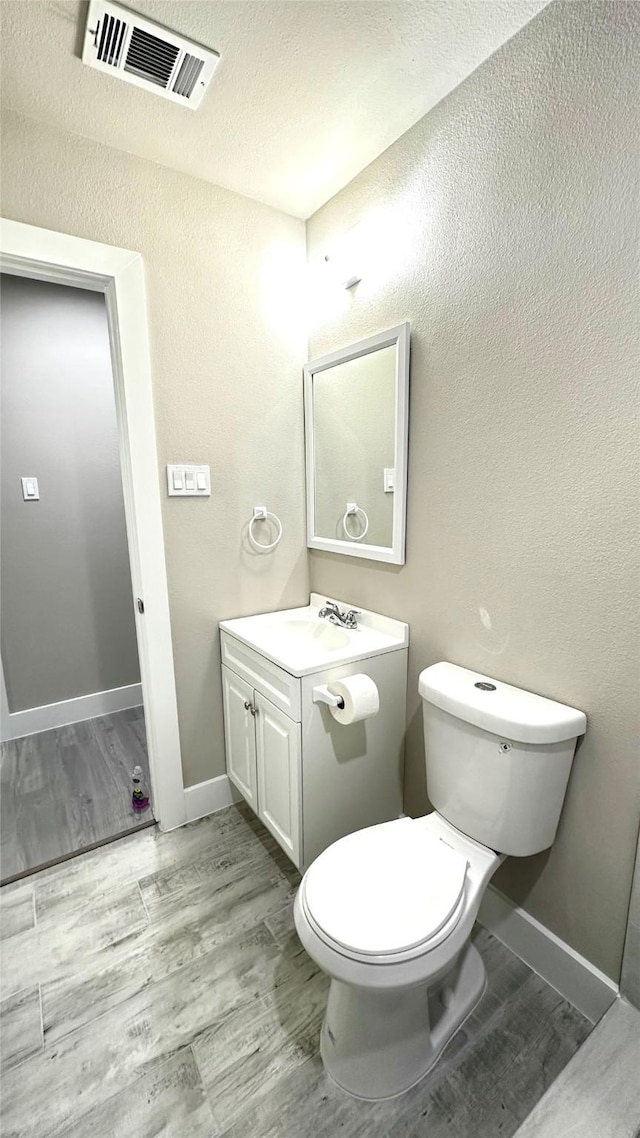 half bathroom with vanity, wood finished floors, visible vents, and baseboards