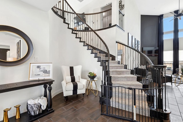 stairway featuring a high ceiling, baseboards, a wall of windows, and wood finish floors